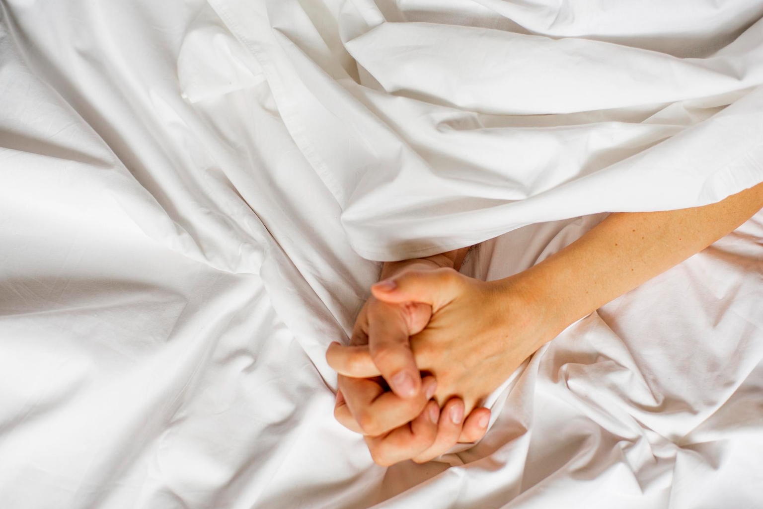 Couple holding hands on white bedsheets